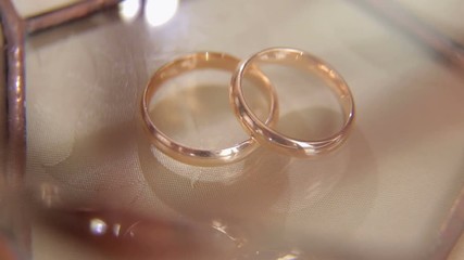Close-up of two wedding rings on a beige background with patches of light.