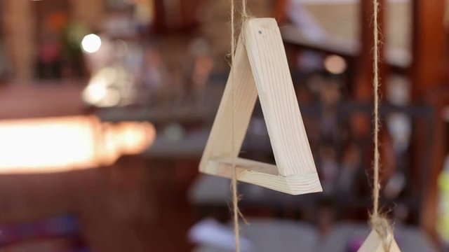 Wooden triangle hanging from a rope outdoors. Wedding decor in rustic stylet.