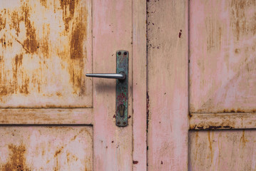 closeup at rusty pink garage door or gate and its handle, old and desolate, damaged paint, scratches
