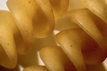 macro closeup of two pieces of hard semoline spiral fusilli pasta, yellow and twisted, above...