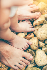 Child's foot learns to walk on pebbles with father together on summer day.