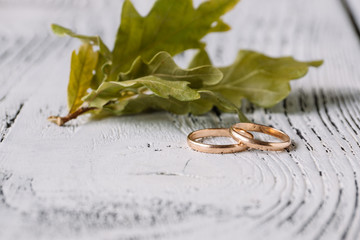 Wedding rings and oak leaves on white wooden background.  Concept of autumn wedding