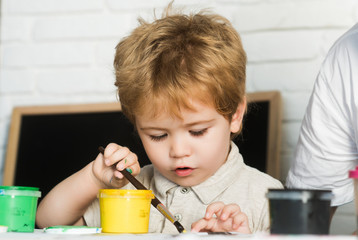 Child development, boy draws paint yellow with brush, interest in art, attention in the drawing class, small schoolboy or kindergarten, picture young artist, master class in art gallery or in studio