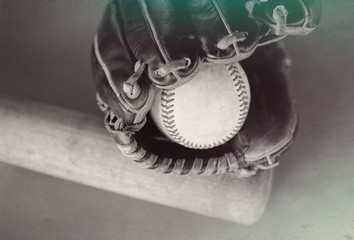 Baseball glove holding ball with vintage wood bat in background.