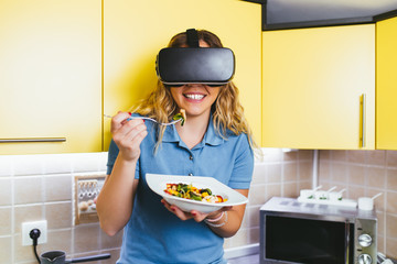Beautiful attractive young woman eating healthy vegetable meal with VR glasses on her. Healthy lifestyle concept. 