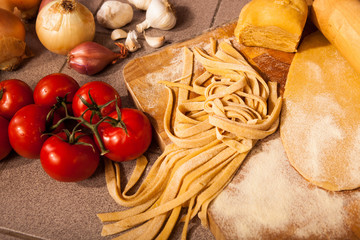 Homemade pasta on cutting board with tomatoes, garlic, and onions