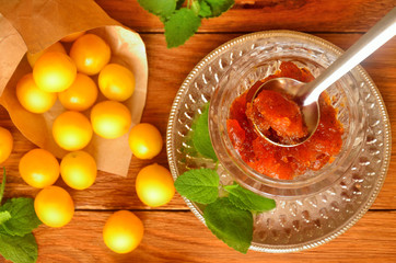 Top view of cherry plum jam and fresh yellow plums on a wooden surface