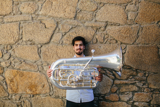 Portrait of musician holding a tuba against a stone wall background