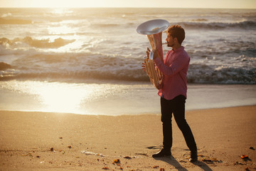 Young man with Tuba musical instrument  on sea shore  outdoor