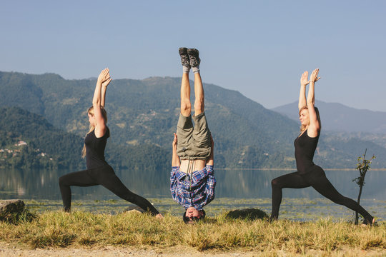 Young yogis doing yoga headstand and standing asana. Beautiful mountain lake landscape background. Complex amazing and funny yoga picture