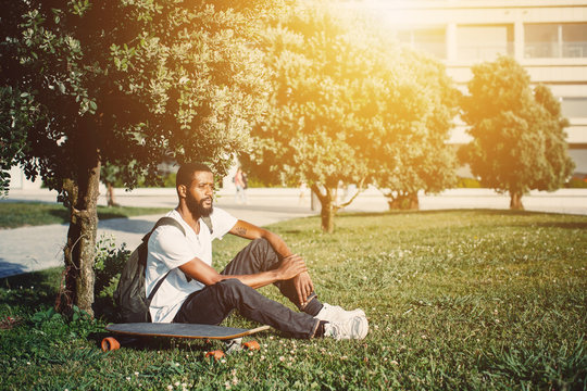 Portrait of man with skate board on the meadow. Mixed race black skin and beard. Summer sport activity outdoor