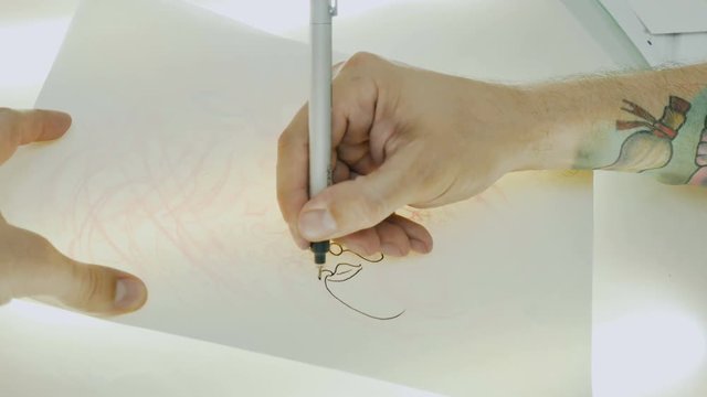 The tattoo artist puts the drawing on the tracing paper on the glass with light