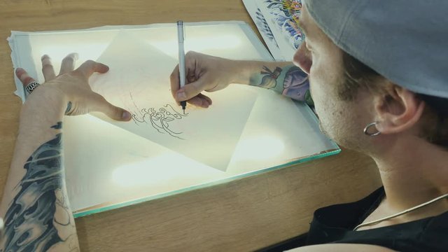 Tattooist draws the sketch on the tracing paper on the glass with light