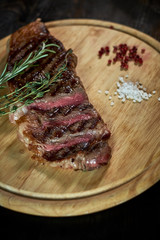 Sliced medium rare grilled steak on rustic cutting board with rosemary and spices , dark rustic metal background, top view, place for text jpg