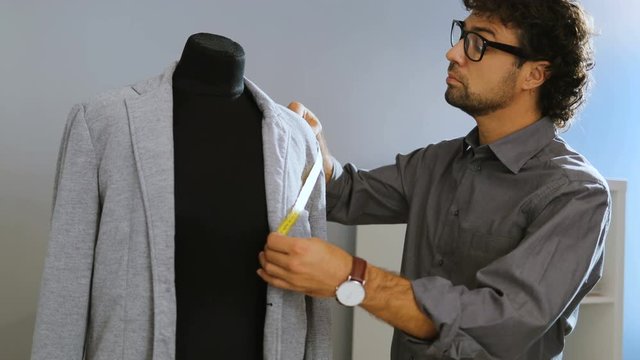 Fashion designer taking measurement from the jacket on the mannequin in the atelier.