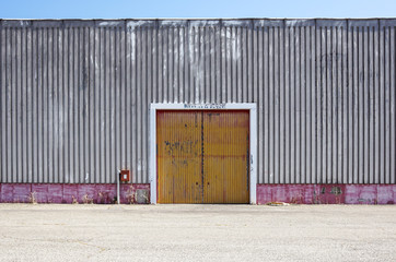 Fototapeta na wymiar The sheet metal factory wall with the entrance door in the industrial park.The red door of the factory building.
