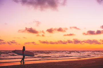 Fototapeta na wymiar Beautiful surfer girl on a beach at warm sunset