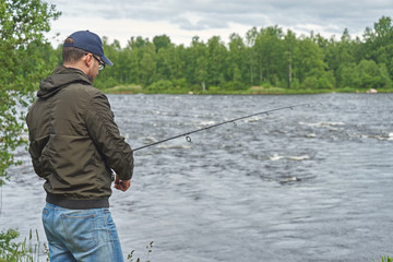 Man fishing with spinning rod in a rapid river.