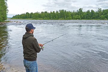 Man fishing with spinning rod in a rapid river.