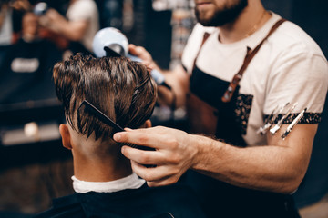 Close-up of a young hipster guy in a barbershop hairdresser cutting hair with scissors and a typewriter, waxing hair, blow-drying. Concept men's place, toned photo. Soft focus.