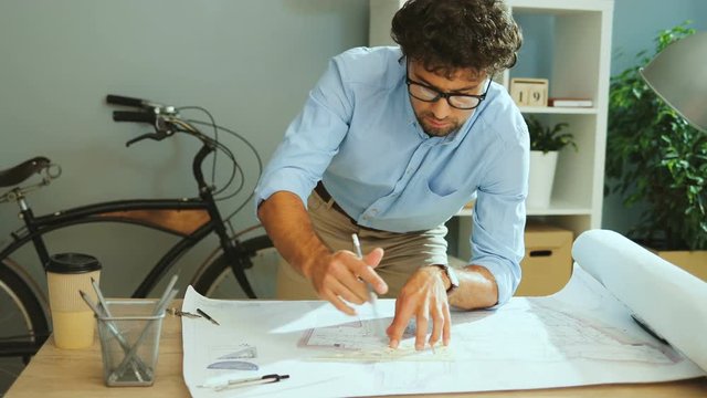 Confident man drawing new line in the new architectural project in his office using pencil and compass.