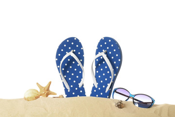Flip-flops and sunglasses on sand against white background. Summer vacation concept