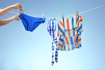 Female hands hanging out beachwear on a line. Summer vacation concept - obrazy, fototapety, plakaty