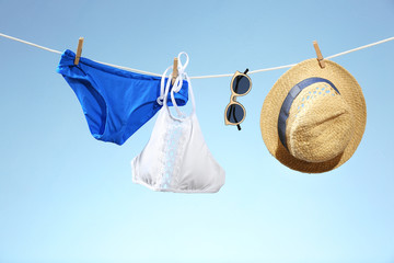 Bikini, hat and sunglasses hanging on rope against light color background. Summer vacation concept