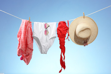 Beachwear, hat and sunglasses hanging on rope against light color background. Summer vacation...