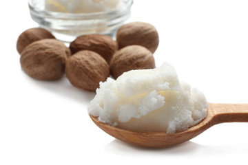 Shea butter in wooden spoon and nuts on white background