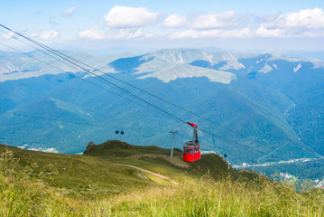 A view to red open cableway cabin over the top of the mountain and beautiful landscapes with blue mountains, green walley, Bucegi natural park, Sinaia, Romania.