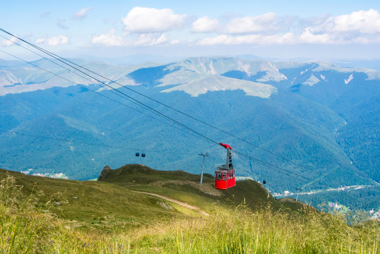 A view to red open cableway cabin over the top of the mountain and beautiful landscapes with blue mountains, green walley, Bucegi natural park, Sinaia, Romania.