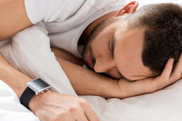 Fototapeta na wymiar close up of man with smartwatch sleeping in bed