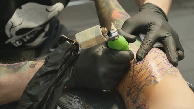 The tattooist is making the tattoo on the man's hand