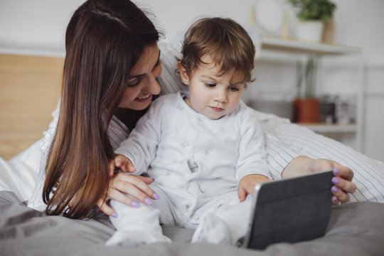 Happy mother using tablet computer with baby boy on bed