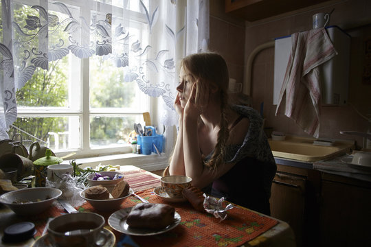 Young thoughtful woman sitting by table at home