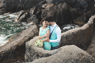 The bride and groom on nature in the mountains near the water. Suit and dress color Tiffany. Kiss and hug.