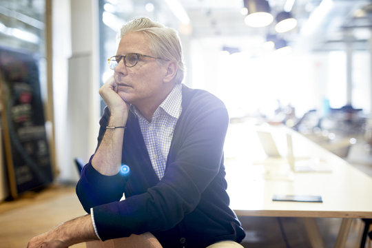 Thoughtful Senior Businessman Looking Away While Sitting In Brightly Lit Office