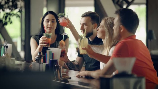 people, leisure, friendship and communication concept - group of happy smiling friends drinking beer and cocktails talking at bar or pub