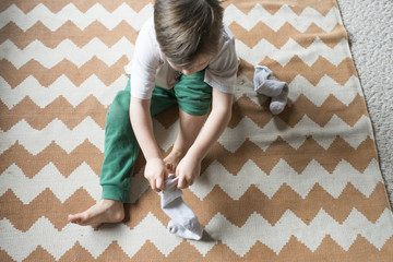 High angle view of boy wearing sock while sitting on carpet at home
