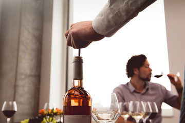 Bartender opening wine bottle while customer tasting in background