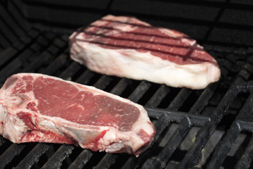 Raw steaks being grilled on a barbecue