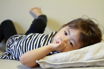 指をくわえて横になる幼児(2歳児)