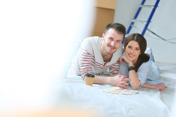 Couple choosing paint colour from swatch for new home lying on wooden floor