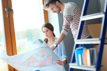 Young couple sitting on the floor and looking at the blueprint of new home