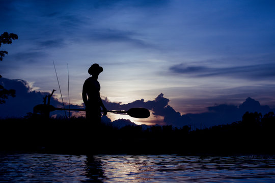 Silhouette of  fisherman standing on boat,hold paddle,on sunset background.
