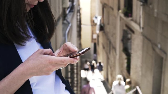 Close up of an unrecognizable young businesswoman texting from her smartphone in a Toledo street. People in the background. Handheld real time close up shot