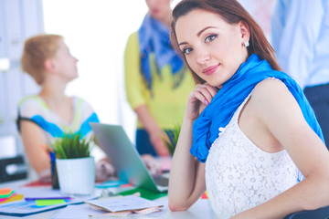 Portrait of attractive female designer sitting on desk in office