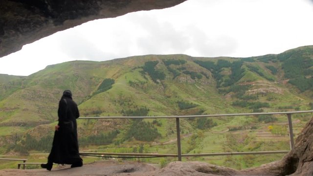 Unrecognizable woman in black clothes goes to the temple  Nun in black clothes near Vardzia cave monastery.