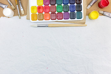 Naklejka premium watercolor paints palette with paintbrushes on gray recycled paper background